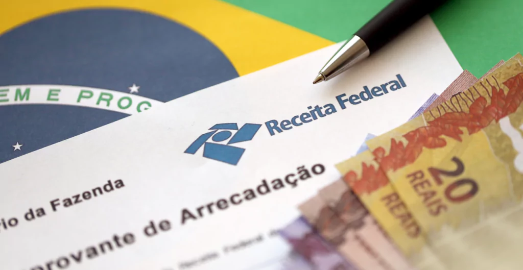 Papel impresso com logo da Receita Federal, notas de vinte e dez reais sobre uma bandeira do Brasil 